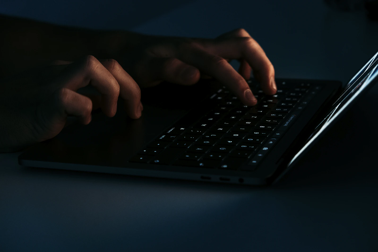 Hands typing on a laptop keyboard in low light